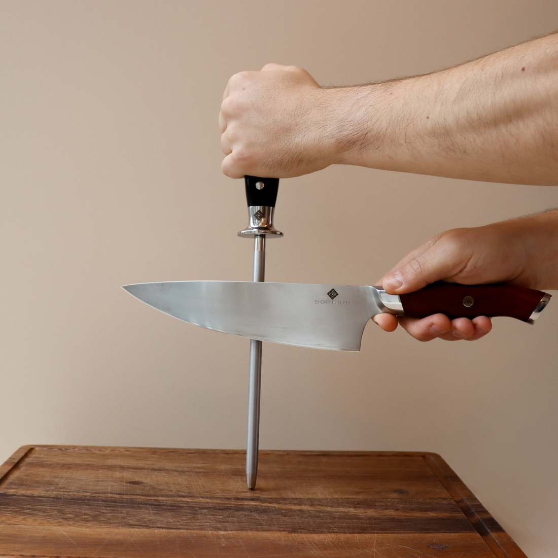 Handen slijpen koksmes met diamant slijpstaaf op houten snijplank tegen lichte achtergrond