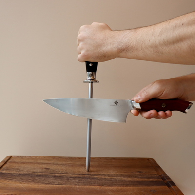 Handen slijpen koksmes met diamant slijpstaaf op houten snijplank tegen lichte achtergrond