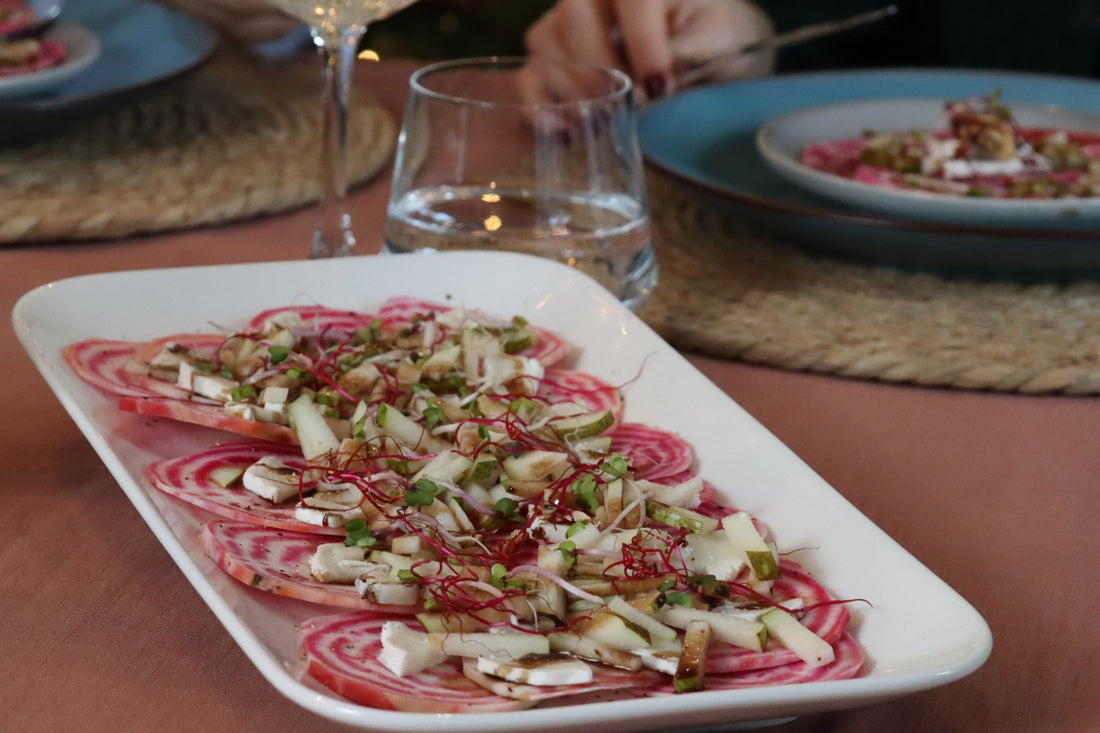 Chioggia bietencarpaccio met peer en geitenkaas op wit bord met champagne