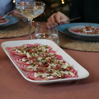 Chioggia bietencarpaccio met peer en geitenkaas op wit bord met champagne