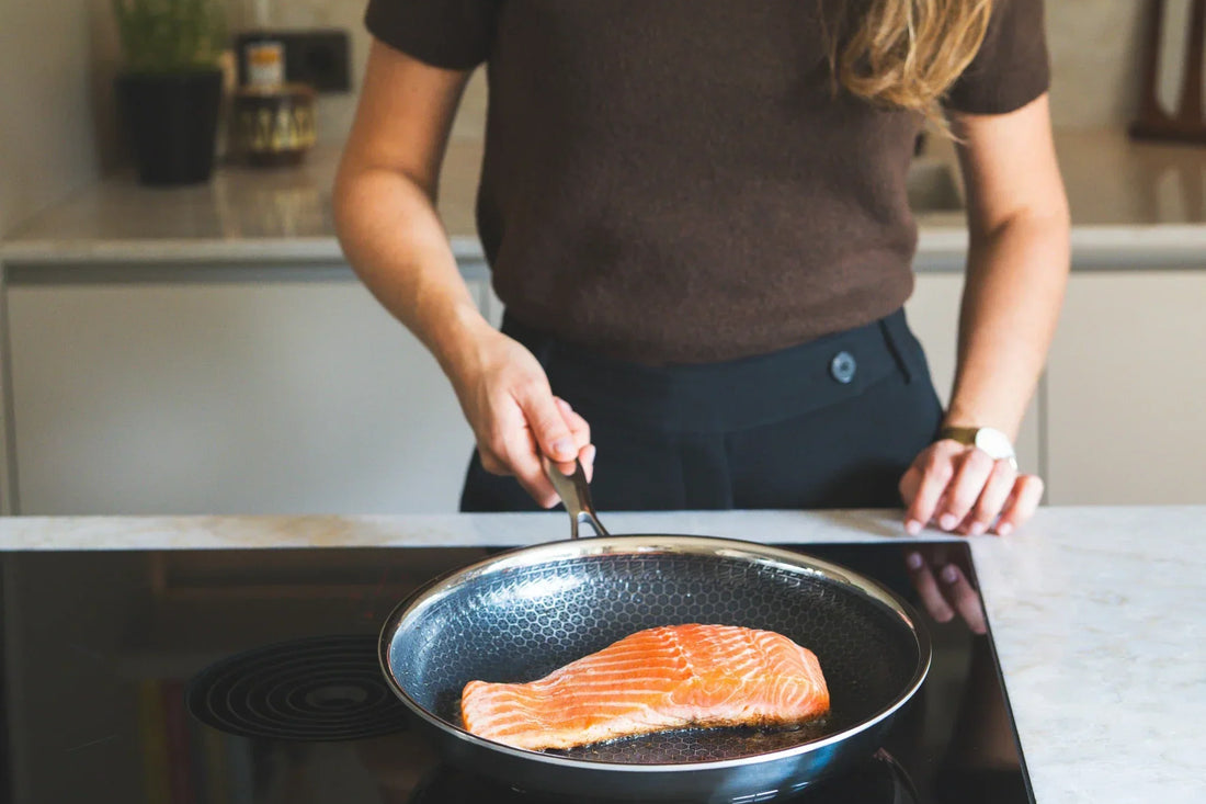 Vrouw bakt zalmfilet in hybride honingraatpan op inductiekookplaat met marmeren werkblad in keuken