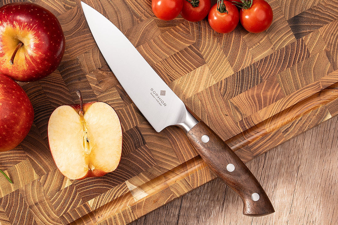 SOPHIOR koksmes 14 cm met walnoothouten handvat op een houten snijplank met appels en trostomaten