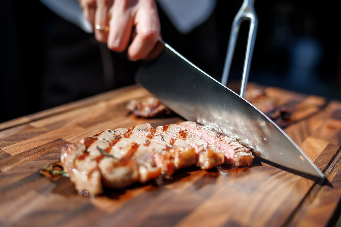 Persoon snijdt rosé gegrilde steak met groot koksmes op kopshouten snijplank in buitenlucht