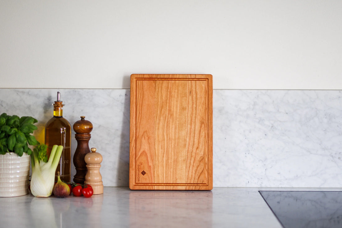 Houten snijplank van kersenhout op marmeren keukenblad met basilicum en olijfolie