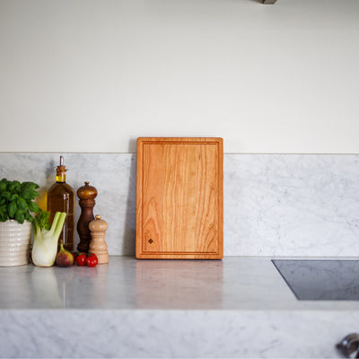Houten snijplank van kersenhout op marmeren keukenblad met basilicum en olijfolie