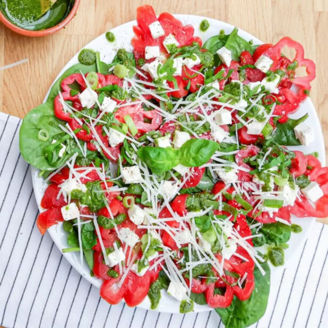 Frisse tomaten carpaccio met spinazie, fetablokjes en pesto-dressing op wit bord