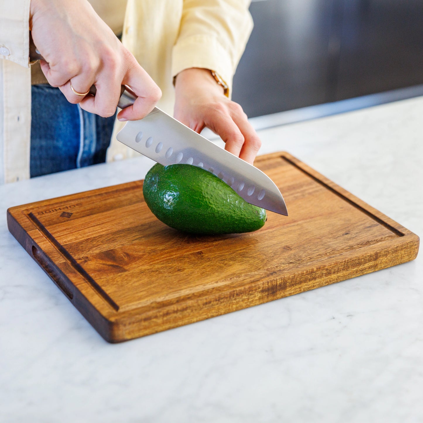 Houten Snijplank Acacia – 35×25×2,5 cm in gebruik tijdens het snijden van een avocado op marmer