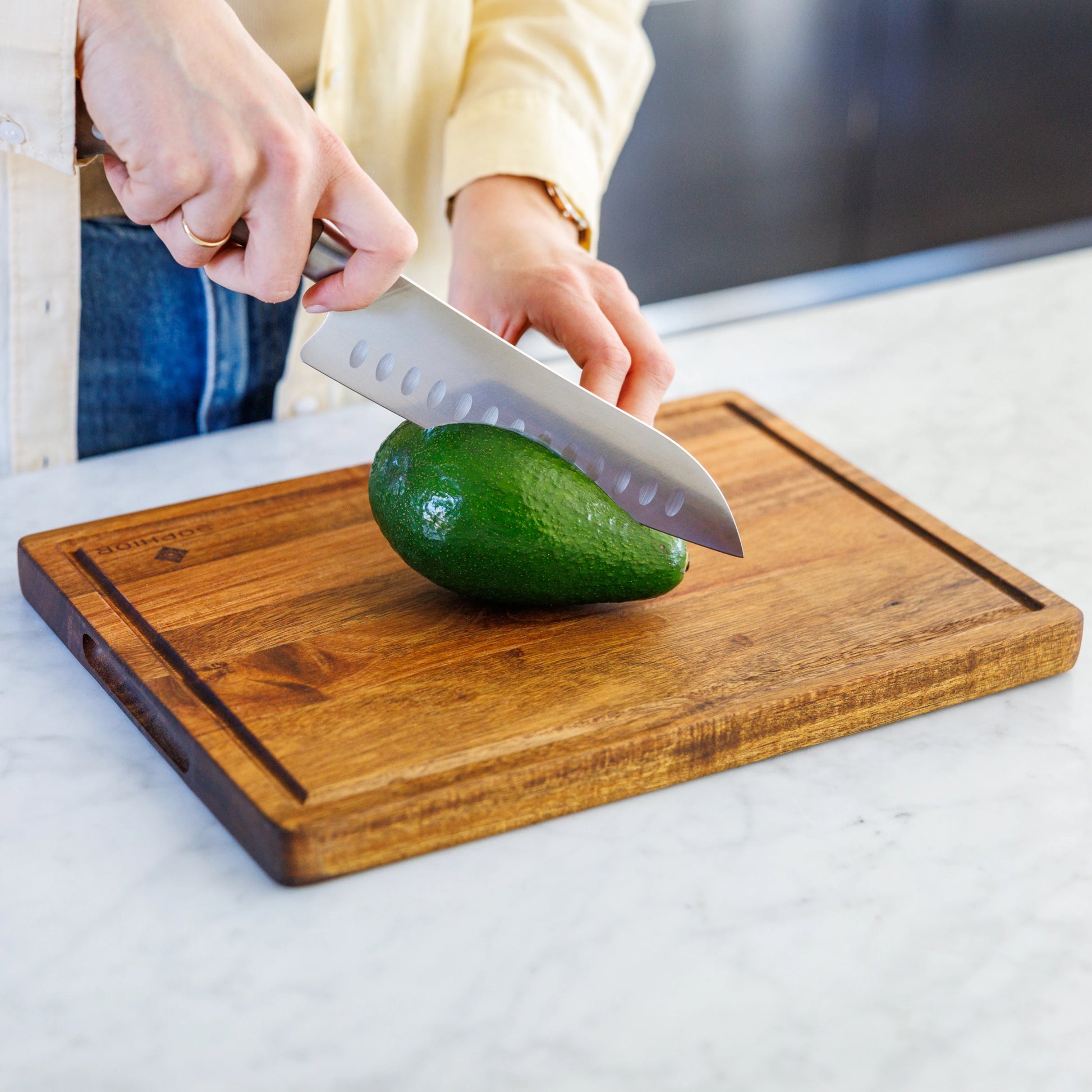 Houten Snijplank Acacia – 35×25×2,5 cm in gebruik tijdens het snijden van een avocado op marmer
