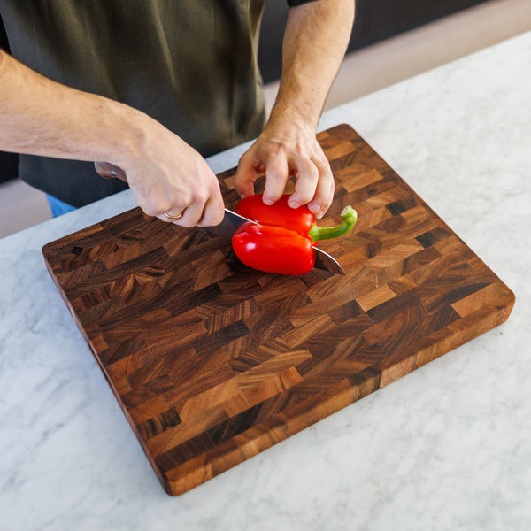 Houten Snijplank Walnoot Kopshout – 45×35×4 cm tijdens het snijden van een rode paprika